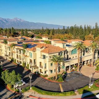 An aerial view of a Mediterranean-style hotel surrounded by lush greenery and distant mountains.