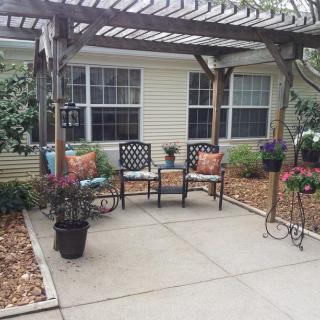 A cozy patio area with a pergola, featuring outdoor seating and surrounded by potted plants.