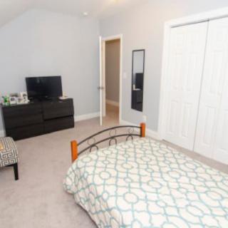 A neatly arranged bedroom with a bed, dresser, television, and closet.