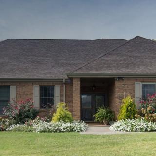 A suburban brick house with well-maintained landscaping and a lush green lawn.