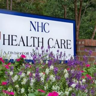 A sign for NHC Health Care surrounded by colorful flowers.