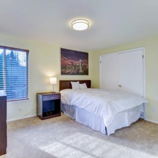 A cozy bedroom with a neatly made bed, nightstand, and a window letting in natural light.