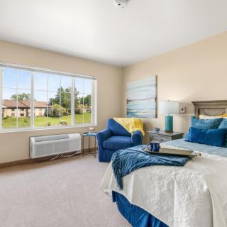 A modern and bright bedroom with blue accents and a large window offering an outdoor view.