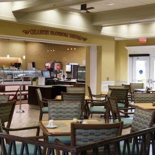 An empty restaurant interior with tables and chairs arranged for dining, featuring a cafe counter in the background.
