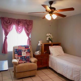 A cozy bedroom with a single bed, ceiling fan, and comfortable chair by the window.