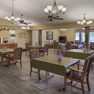 A well-lit dining area with multiple tables and chairs, decorated with chandeliers and ceiling fans.