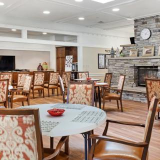 A cozy dining area with patterned chairs and round tables, featuring a stone fireplace and warm wooden flooring.