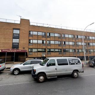 A city street featuring a multistory brick building with parked vehicles.
