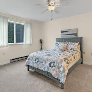 A cozy bedroom with a bed covered in a patterned duvet, a window with curtains, and a ceiling fan.