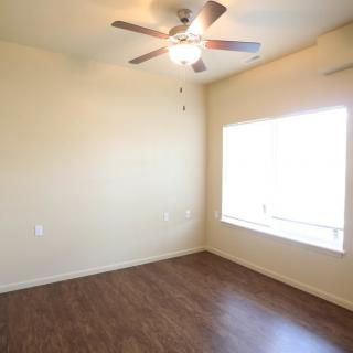 A bright, empty room with wood flooring and a ceiling fan.