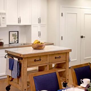 A cozy kitchen featuring a wooden island with a fruit bowl and white cabinetry.