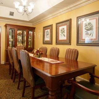 A classic dining room with an elegant wooden table, upholstered chairs, and framed artwork on the walls.