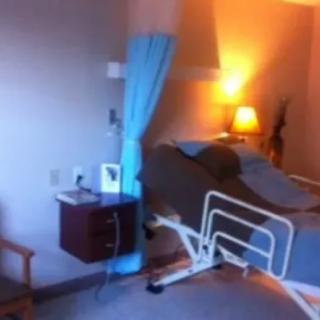 A hospital room with a bed, nightstand, and chair.