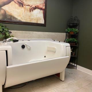 A modern bathroom with a white bathtub and green walls, featuring artwork and plants for decor.
