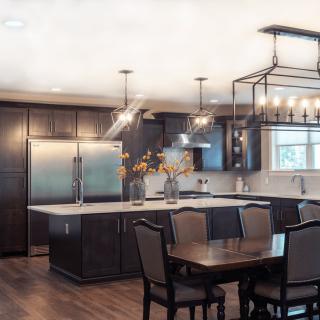 A modern kitchen with an island counter and dining area, featuring dark cabinets and stainless steel appliances.