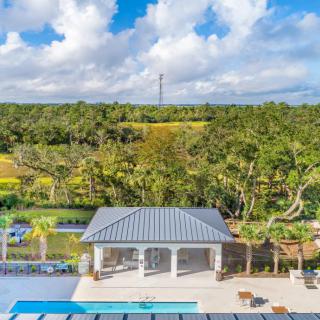 A modern house with a pool surrounded by lush greenery and a scenic landscape under a partly cloudy sky.