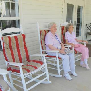 Two elderly individuals sitting on rocking chairs on a porch.