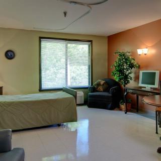 A well-lit hospital room with a bed, desk, and television near a window.