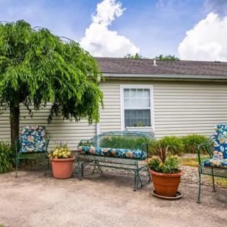 A cozy patio with outdoor seating, surrounded by potted plants and a well-kept garden area in front of a house.