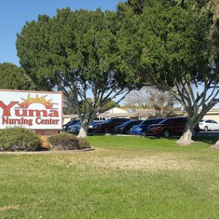 Yuma Nursing Center with a vibrant sign surrounded by lush trees and a parking area.