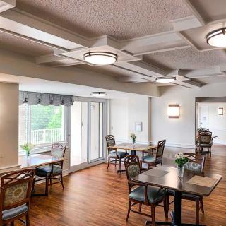 A well-lit dining room with multiple tables and chairs, featuring wood flooring and large windows.
