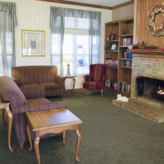 A cozy living room with a fireplace, sofa, chairs, and bookshelves.