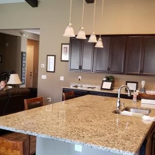 A modern kitchen featuring a large granite countertop island with pendant lighting and dark wood cabinets.