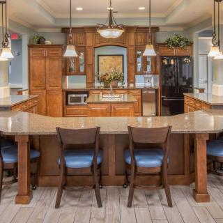 A modern kitchen with wooden cabinets, a spacious island counter, and bar stools, illuminated by pendant lighting.
