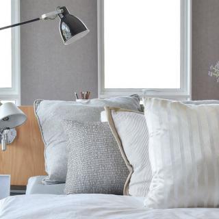 A modern and cozy bedroom with a neatly arranged bed, featuring stylish pillows and a sleek lamp.