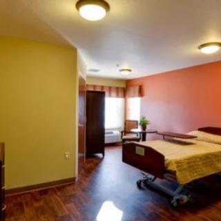 A modern hospital room featuring a single patient bed with wooden flooring and warm lighting.