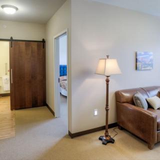 A cozy living room area with a sofa and a floor lamp, adjacent to a hallway leading to another room.