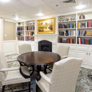 A cozy library room with a round table and upholstered chairs surrounded by bookshelves.