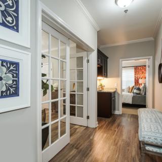 A modern hallway with wood flooring, featuring French doors, artwork on the walls, and elegant lighting.