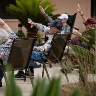 A group of seniors participating in an outdoor exercise session while seated in chairs.