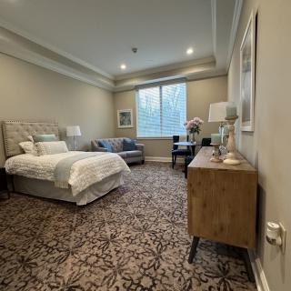 A modern bedroom with stylish decor, featuring a bed, sitting area, and large window.