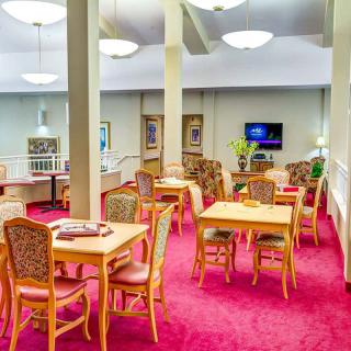 A spacious lounge area with tables and chairs on a red carpet, featuring bright lighting and a television.