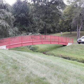 A vibrant red bridge crosses over a small stream in a serene park setting.