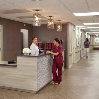 Nurses conversing at a hospital reception desk in a clinical setting.