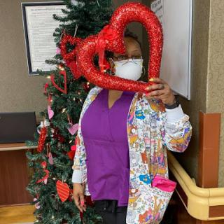 A cheerful staff member celebrating the holiday season with festive decorations and a heart-shaped prop.