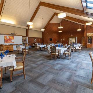A spacious dining room with neatly arranged tables and chairs under a wooden ceiling.