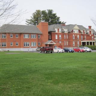 A historic brick building with a well-maintained lawn and parked cars in front.
