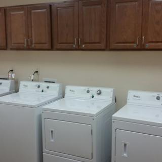 A row of washing machines and dryers beneath wooden cabinets in a laundry room.