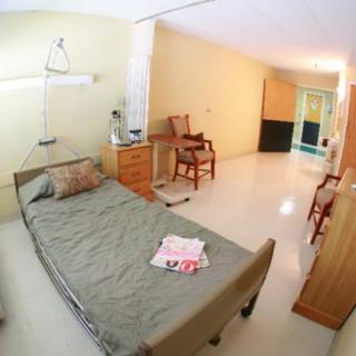 A clean and spacious hospital room with a bed and wooden furniture.