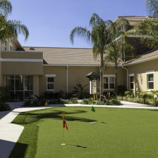 A sunny courtyard with a putting green surrounded by palm trees and buildings.