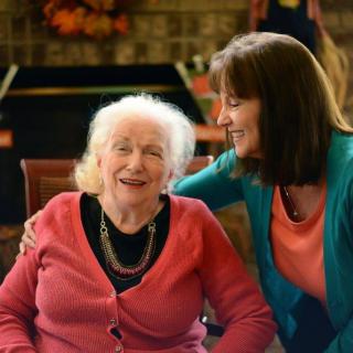 An elderly woman and a younger woman share a joyful moment indoors.