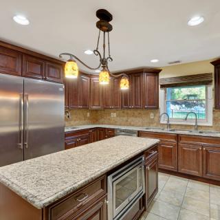 A modern kitchen featuring a central island with granite countertops, wood cabinets, and stainless steel appliances.