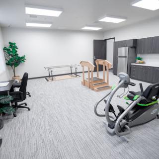 A well-equipped therapy room featuring exercise equipment, office furniture, and bright lighting.