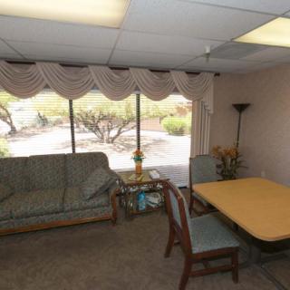 A small office meeting room featuring a sofa, a table with chairs, and large windows with curtains.