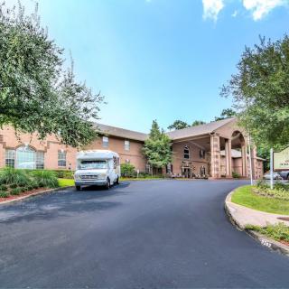 A building with a driveway and a parked van near the entrance, surrounded by trees.