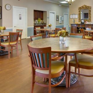 A well-lit dining area with wooden tables and chairs, decorated with flowers.
